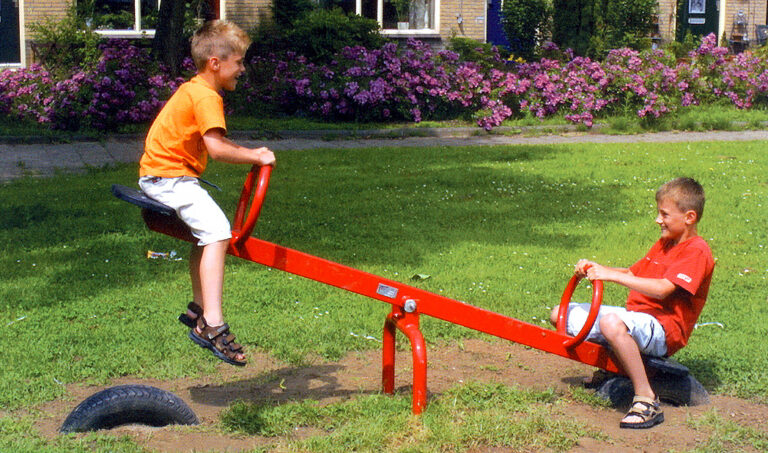Kleuter speelt op metalen wip in primaire kleur in speeltuin
