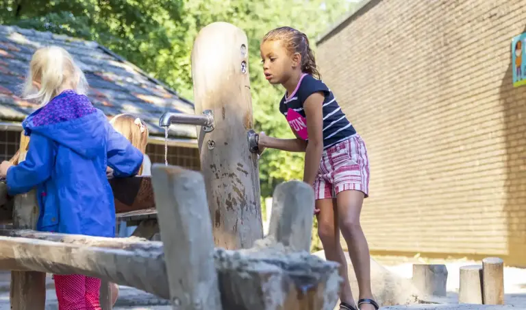 Kind tapt water bij robinia watertappunt op schoolplein