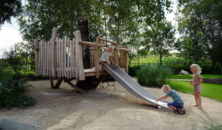 Boomvlonder met glijbaan speeltoestel met jonge kinderen op een speelplek