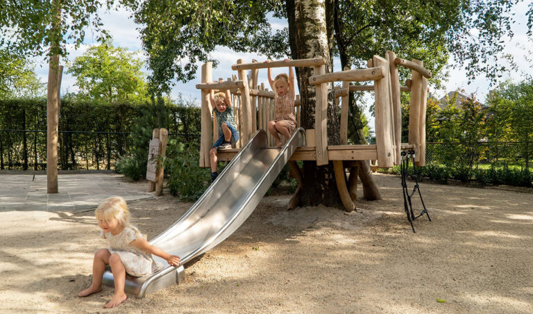 Boomvlonder met glijbaan speeltoestel met jonge kinderen op een schoolplein