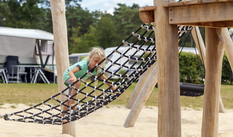 Kind klimmend in klimnet van een groot houten speeltoestel op recreatiepark