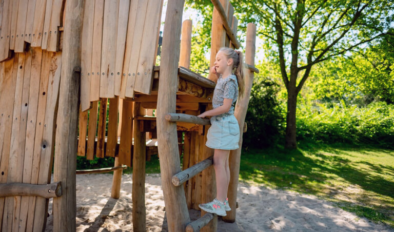 Spelend kind op een speeltoestel met speelhuisje en schommel