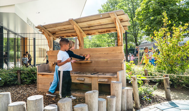 Jongere kinderen spelen met modderkeuken op het schoolplein voor de onderbouw