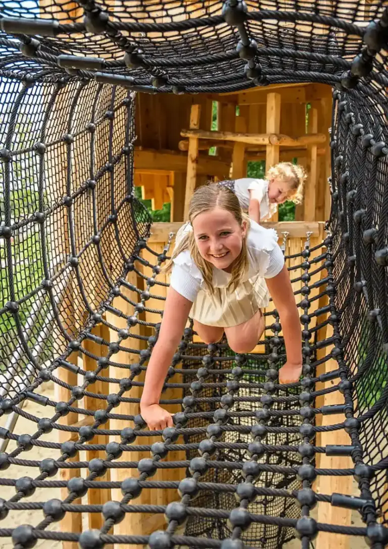 Kind kruipt door tunnelnet in houten speelcombinatie